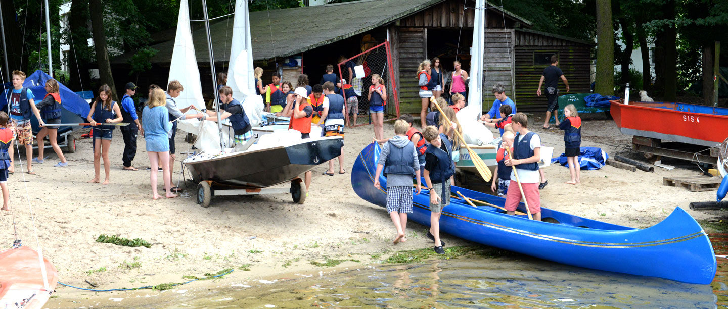 Viele Schüler und Boote stehen auf dem Strand neben dem Fährhaus.