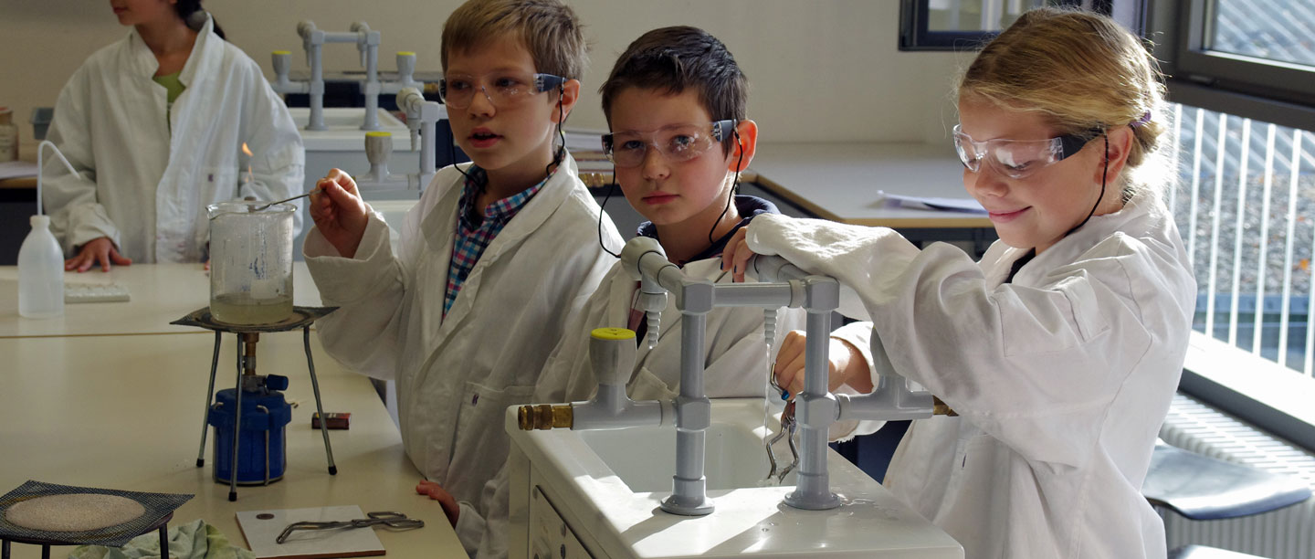 3 Junge Schüler experimentieren im Chemieraum.